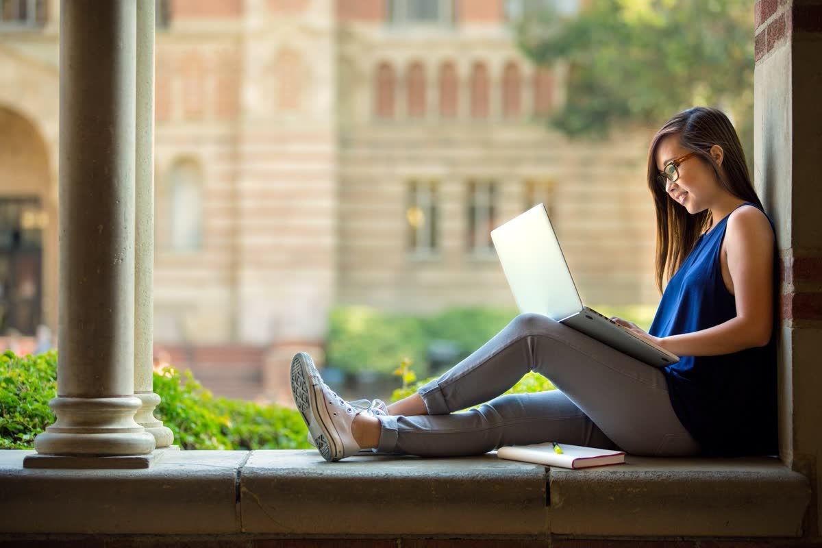 College student working on a laptop outside a campus building